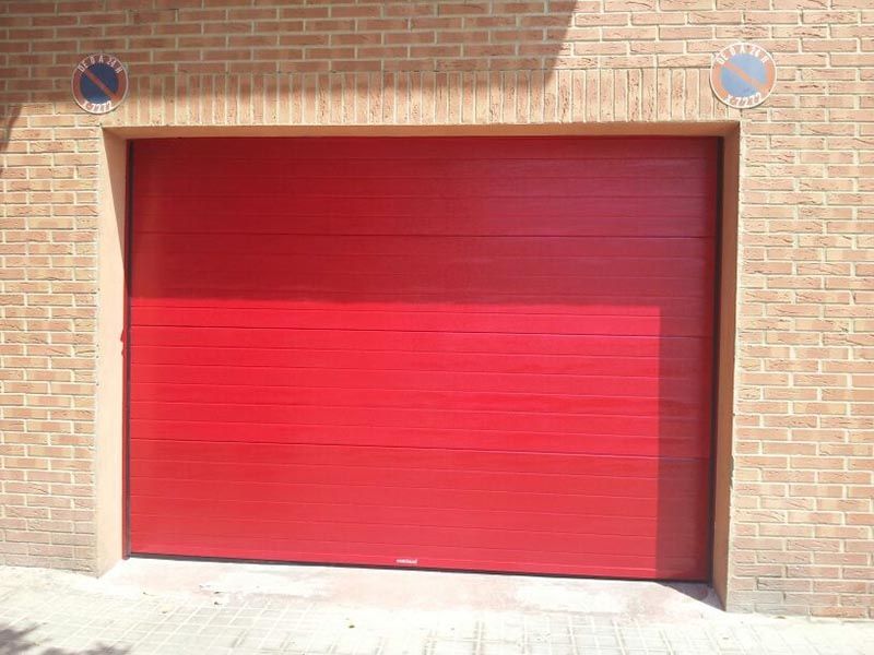 Una puerta de garaje roja está en un edificio de ladrillo.