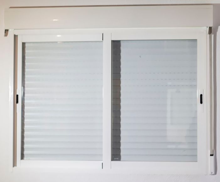 Una ventana blanca con contraventanas está apoyada sobre una pared blanca.