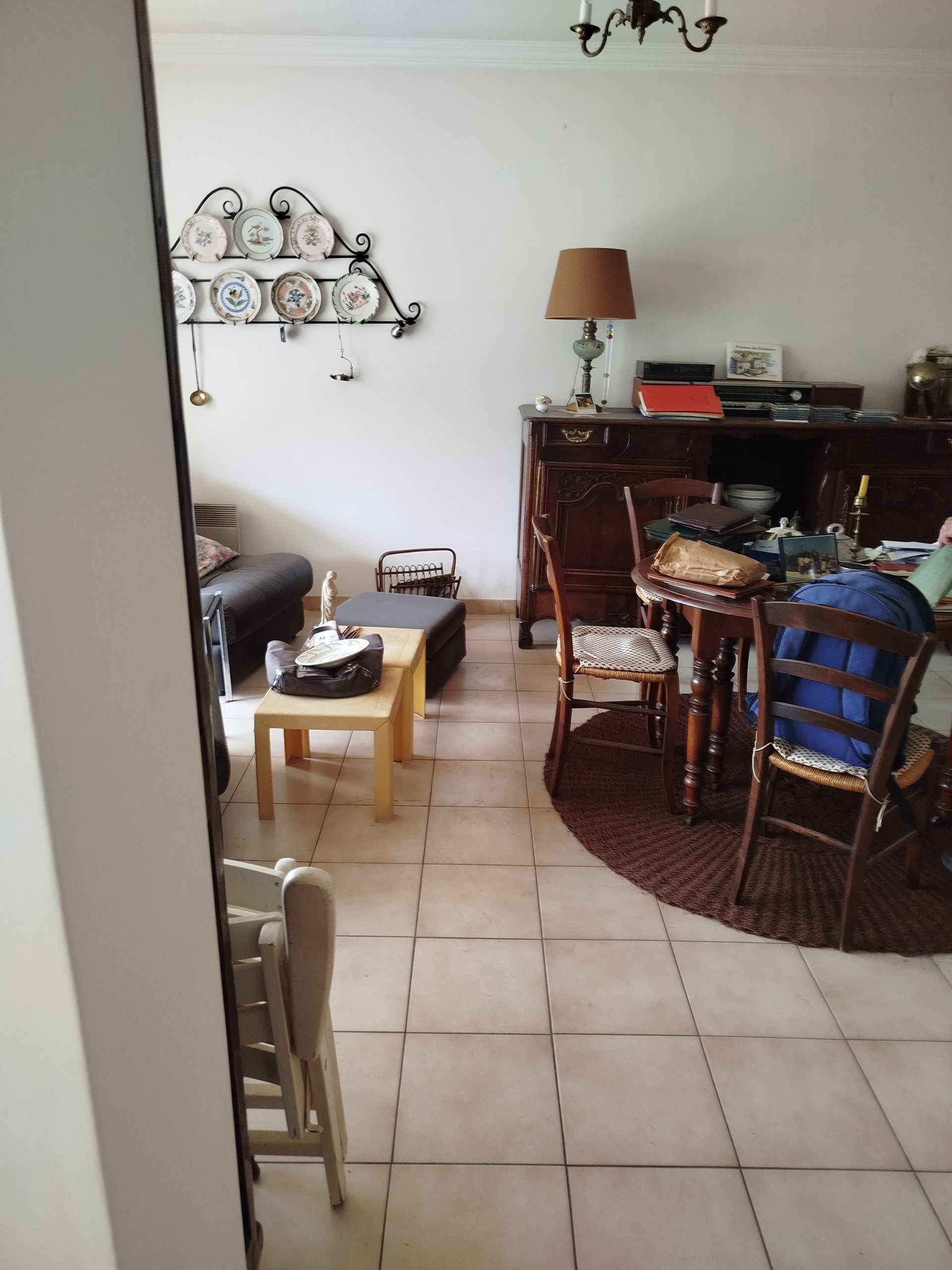 Salon avec meubles en bois, sol carrelé beige clair et mur décoratif d'assiettes.