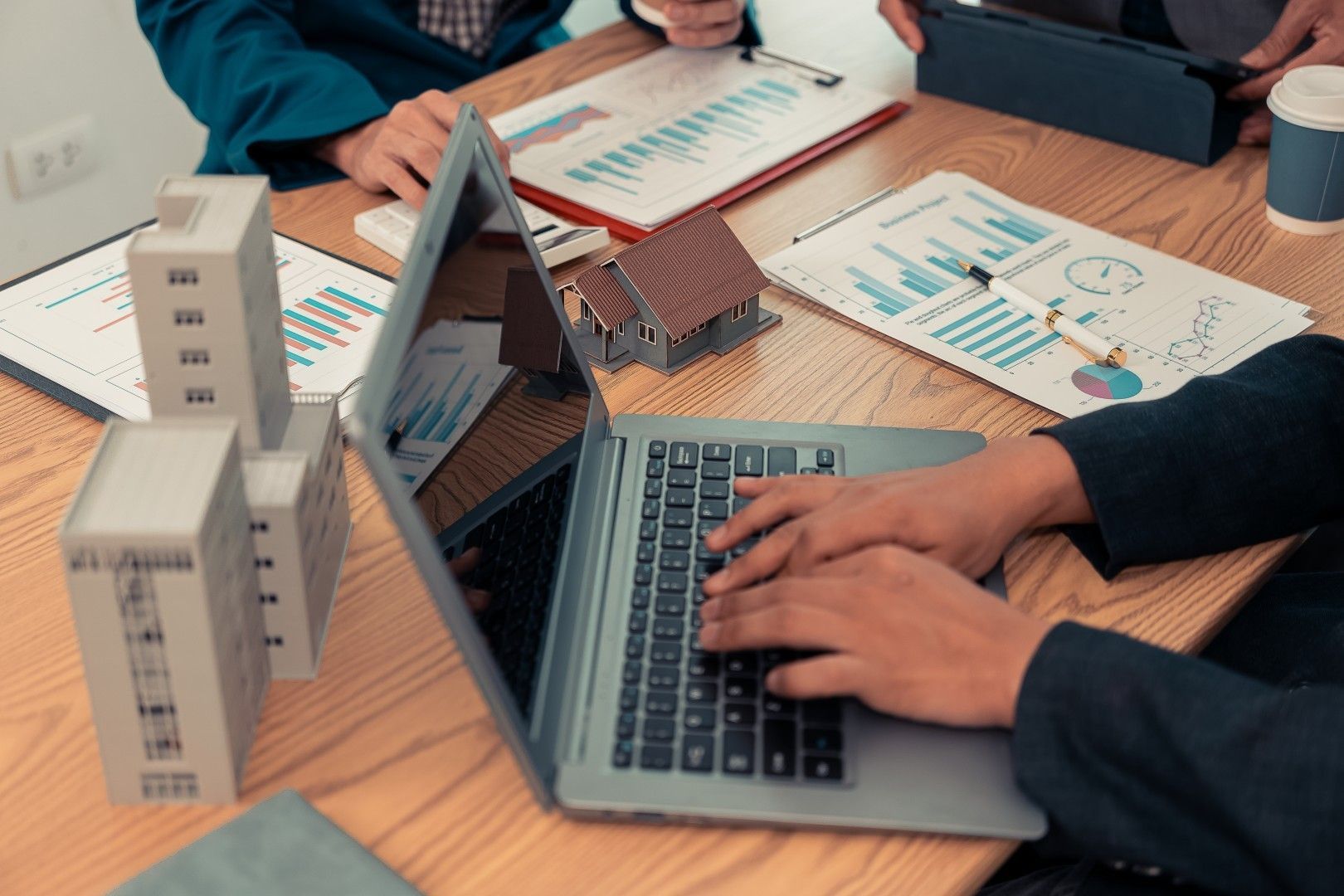 Des personnes collaborent autour d’un ordinateur portable, avec des maquettes d’architecture et des documents sur une table de réunion
