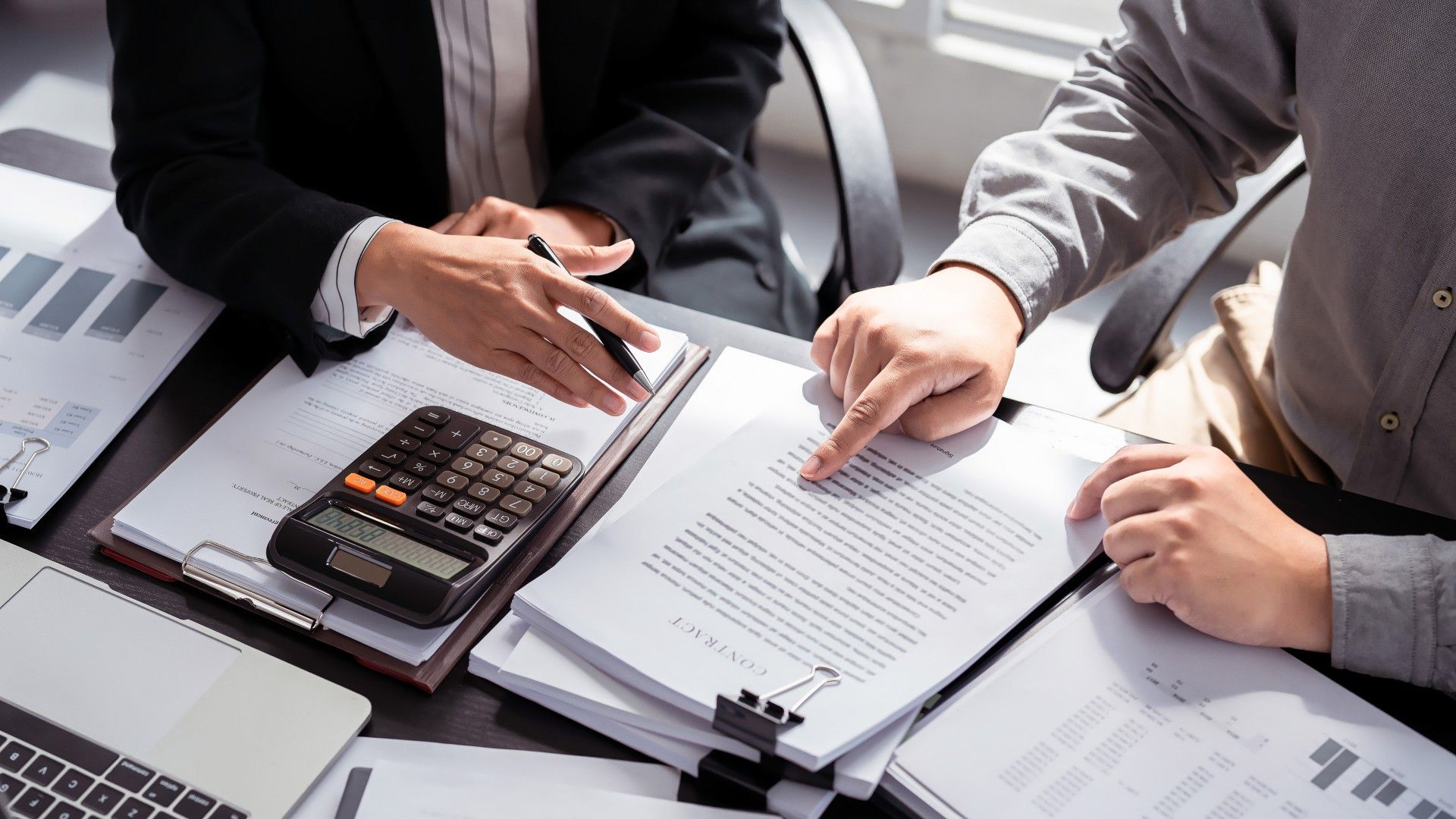Deux personnes en tenue professionnelle examinent des documents financiers avec une calculatrice, assises à un bureau