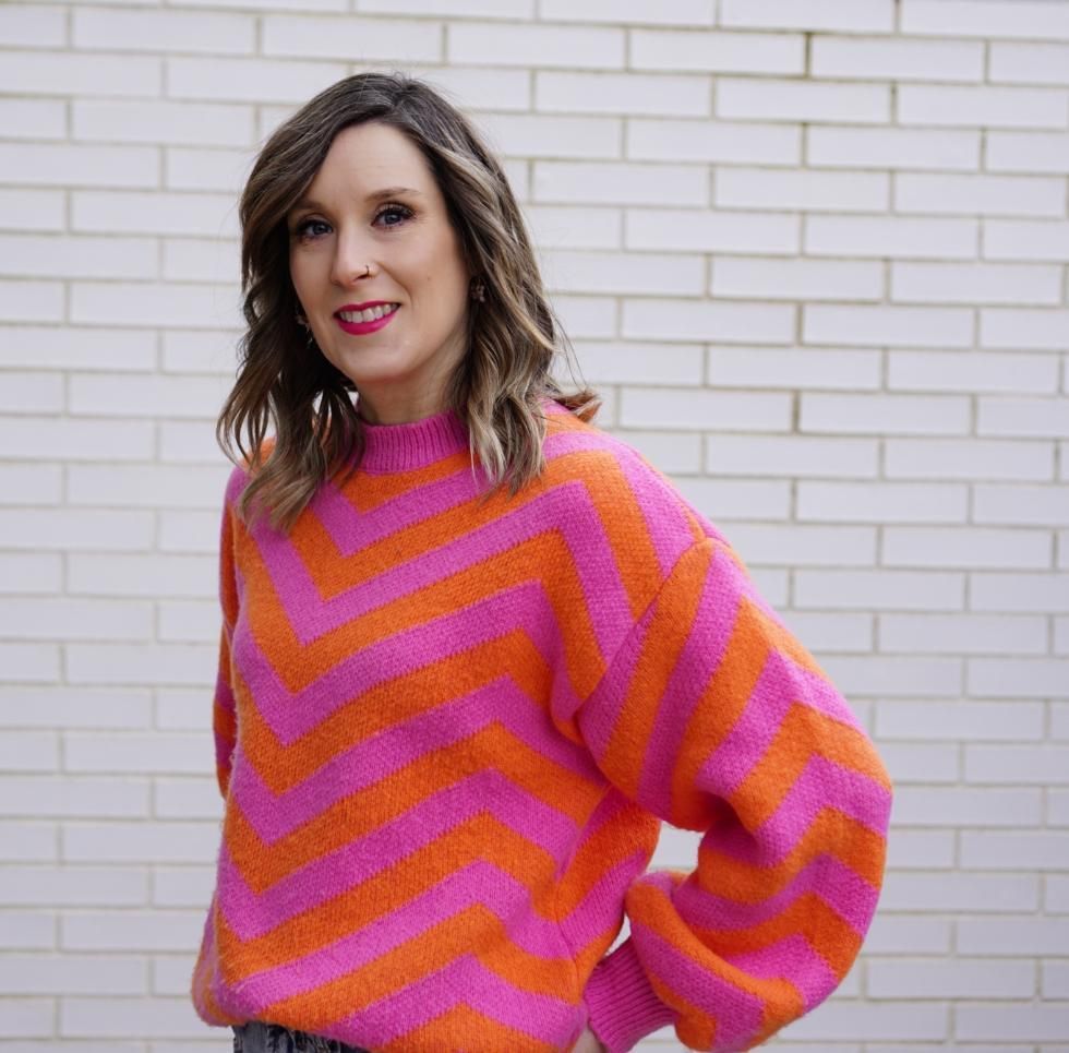 Mujer de cabello largo y castaño, con un vestido rosa y un collar, sonriendo.