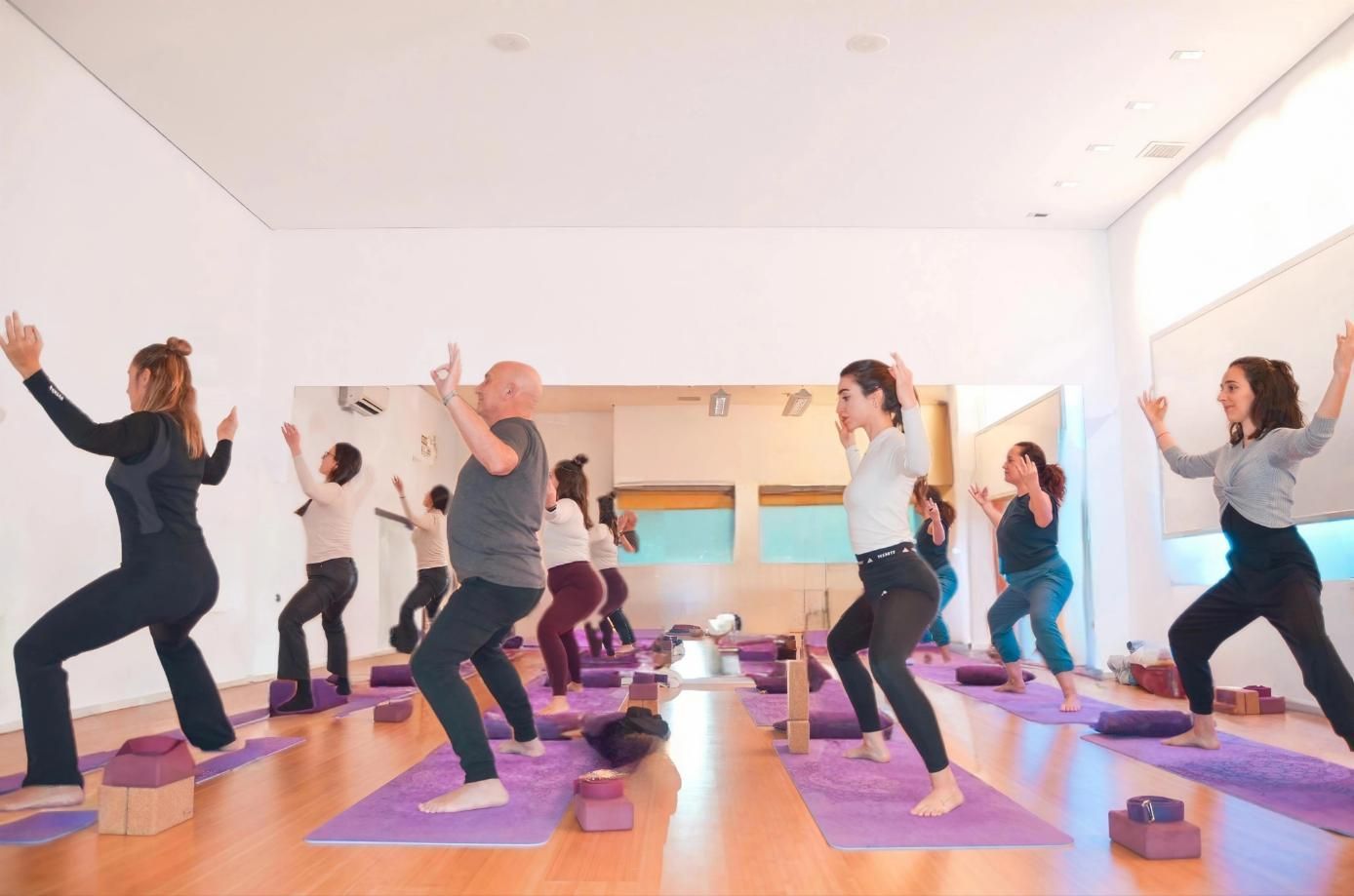 Mujeres en ropa deportiva haciendo una pose de plancha lateral sobre colchonetas moradas en un estudio.