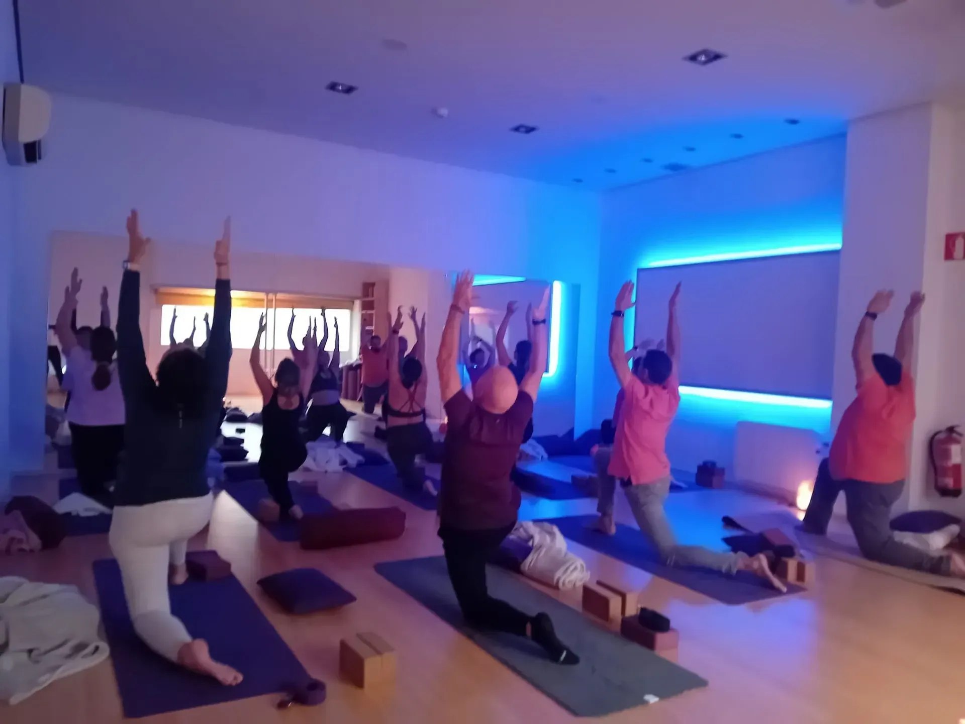 Cinco personas en un estudio de yoga, sentadas sobre colchonetas moradas, con los brazos detrás de la espalda.