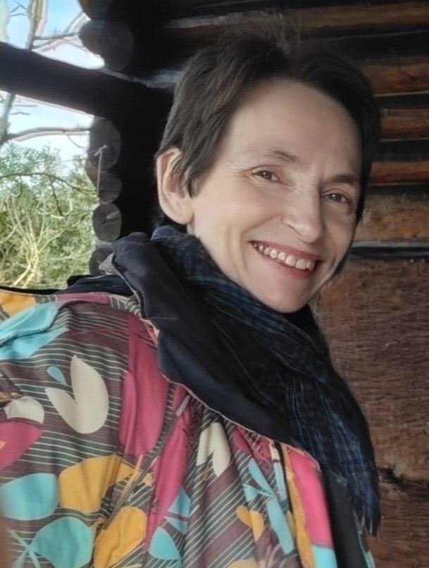 Mujer de cabello largo y castaño, con un vestido rosa y un collar, sonriendo.