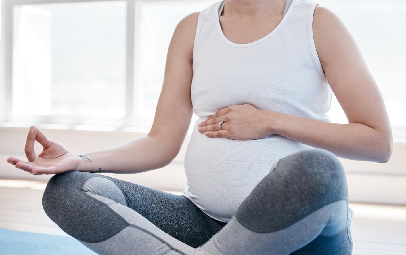 Persona embarazada sentada en una pose de yoga, con las manos en un mudra, sobre una colchoneta azul.
