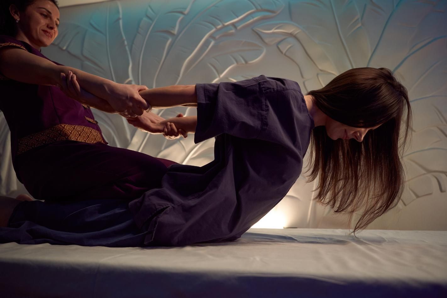 Cinco personas en un estudio de yoga, sentadas sobre colchonetas moradas, con los brazos detrás de la espalda.