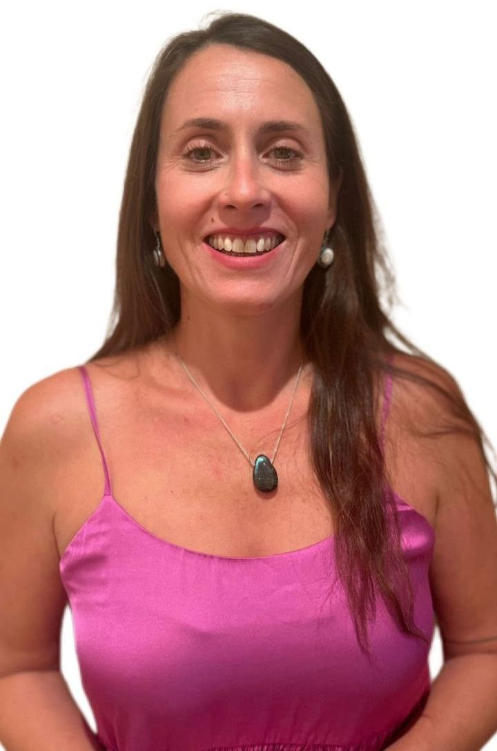 Mujer de cabello largo y castaño, con un vestido rosa y un collar, sonriendo.