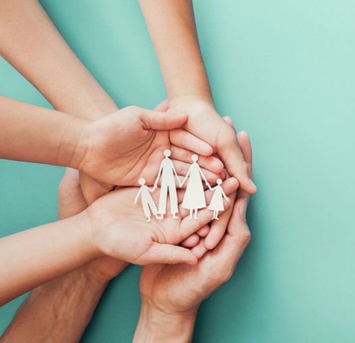 Manos ahuecando una familia recortada en papel, fondo turquesa.