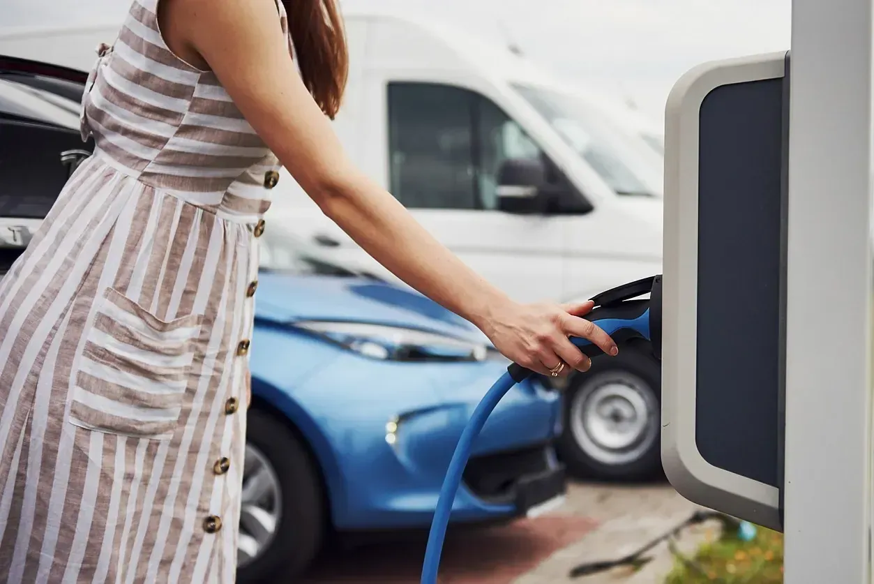 Una mujer está cargando su coche eléctrico en una estación de carga.