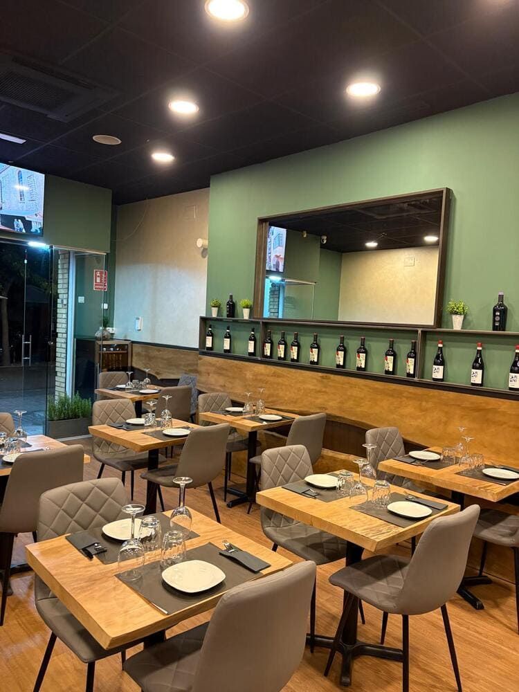 Cafetería moderna vacía con mesas de madera, sillas grises y un gran espejo de pared.