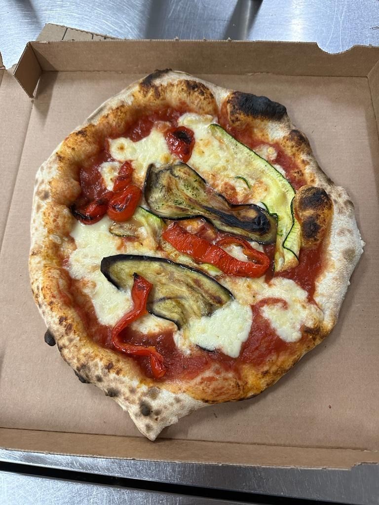 Pizza pequeña en una caja de cartón con queso fundido, tomates y verduras asadas.