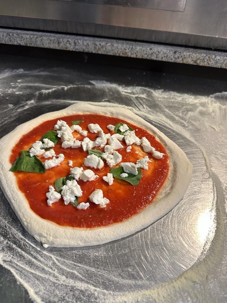 Pizza sin hornear sobre una superficie enharinada, cubierta con salsa de tomate, albahaca y queso desmenuzado.