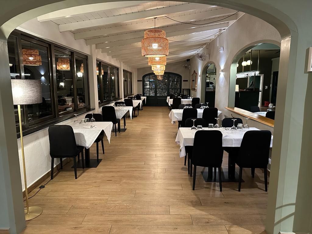 Elegante comedor de restaurante con manteles blancos, sillas negras y lámparas colgantes de luz cálida.