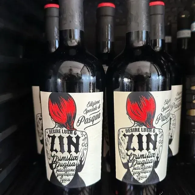 Dos botellas de vino con etiquetas blancas y logotipos de rosas rojas en un estante de la tienda.