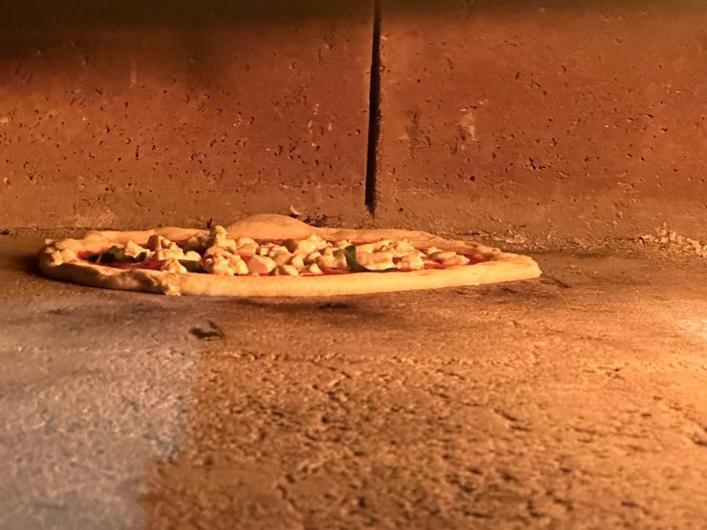 Una pizza horneándose en un suelo de piedra dentro de un horno de ladrillo con un resplandor anaranjado.