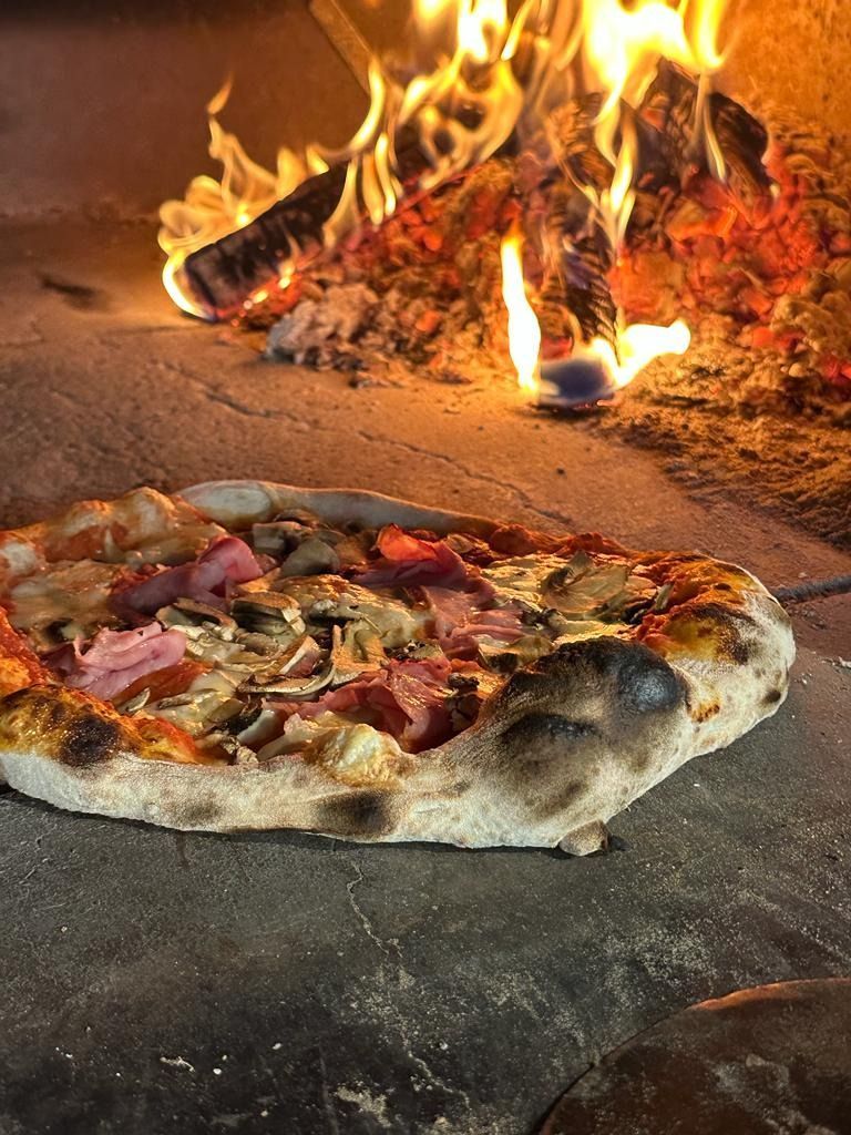 Pizza cocinada en horno de leña con llamas visibles y una corteza crujiente.