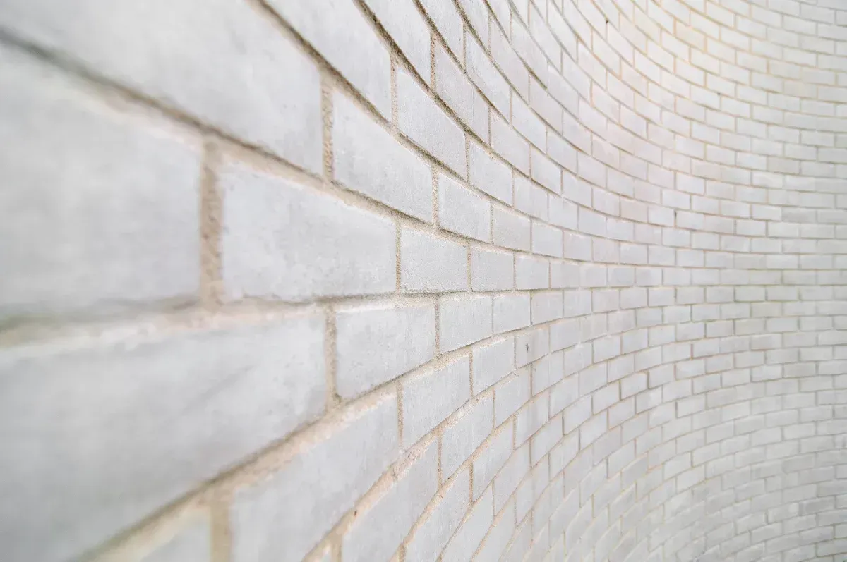 Pared de ladrillo blanco curvada, vista en perspectiva, con juntas de mortero visibles.