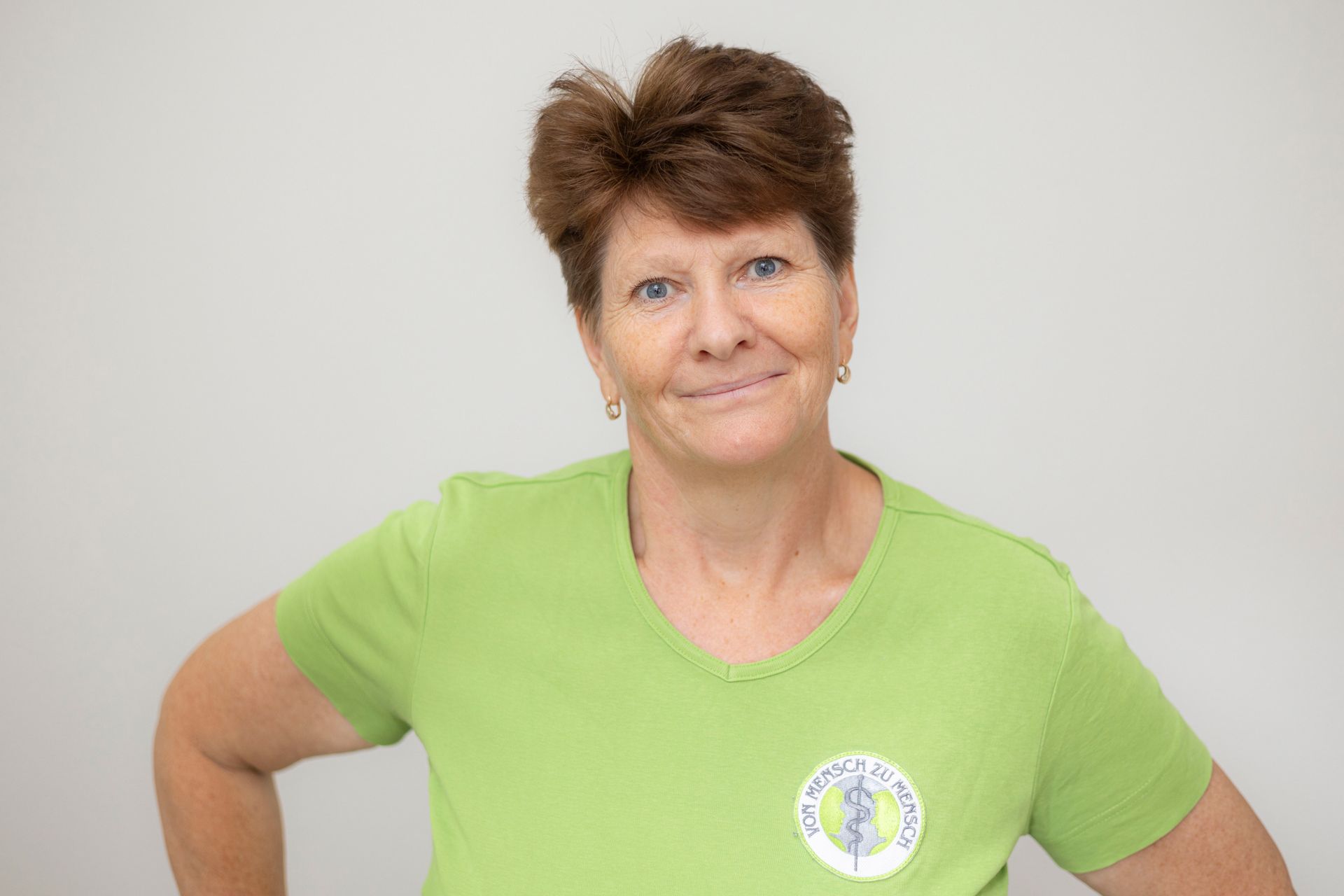 Eine Frau in einem grünen T-Shirt steht mit den Händen in den Hüften da und lächelt.