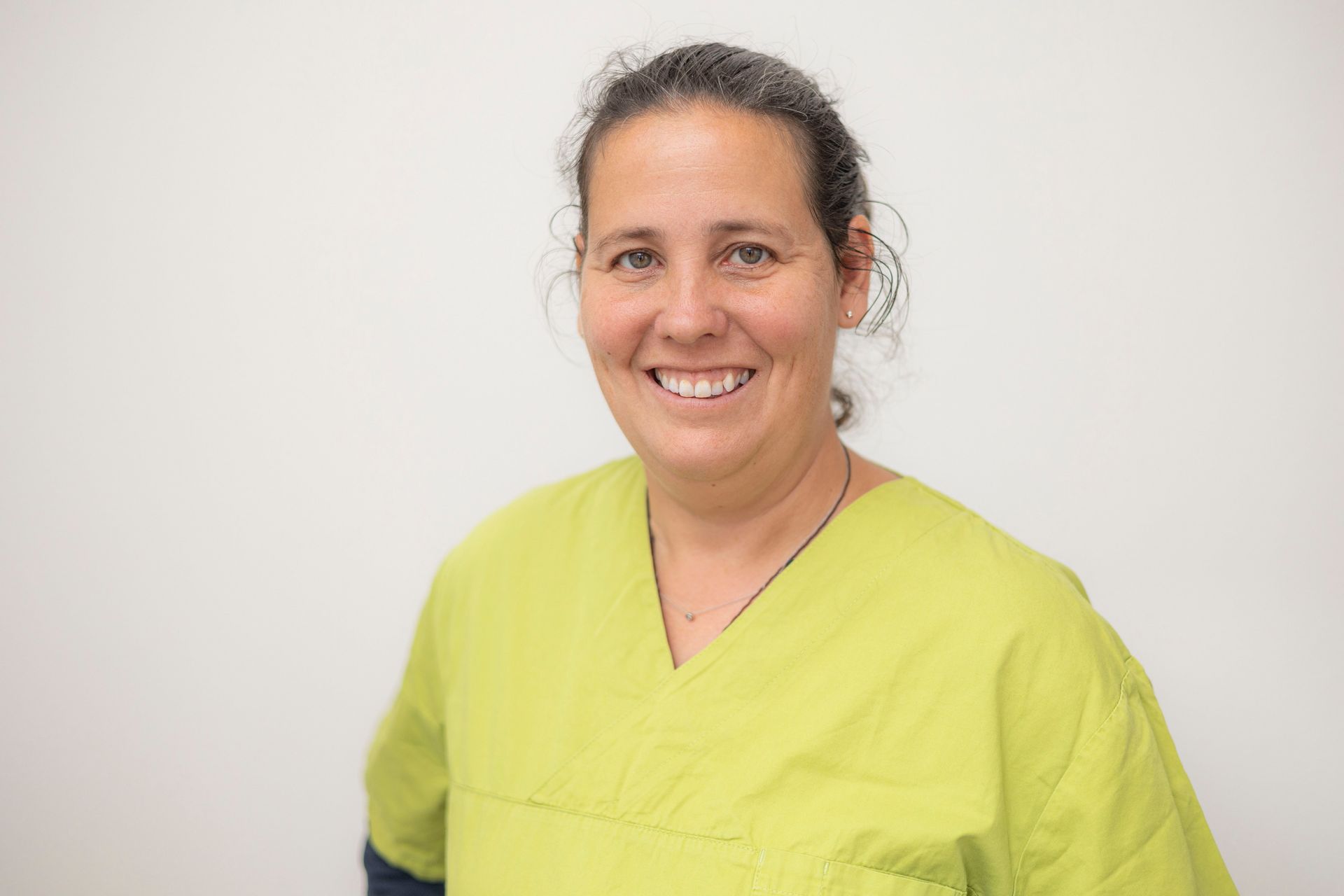 Eine Frau in einem grünen OP-Kittel lächelt in die Kamera.