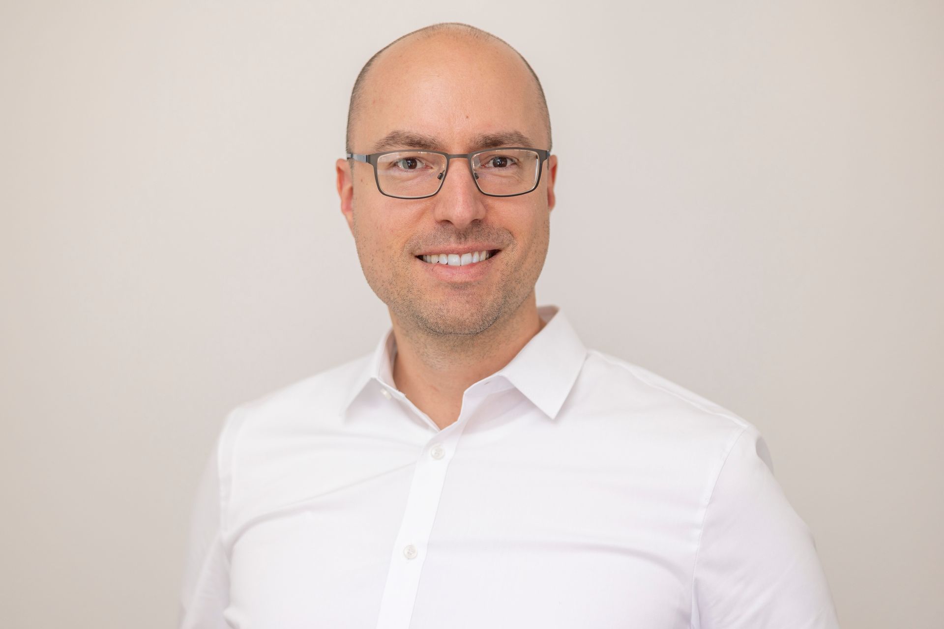 Ein kahlköpfiger Mann mit Brille und weißem Hemd lächelt in die Kamera.