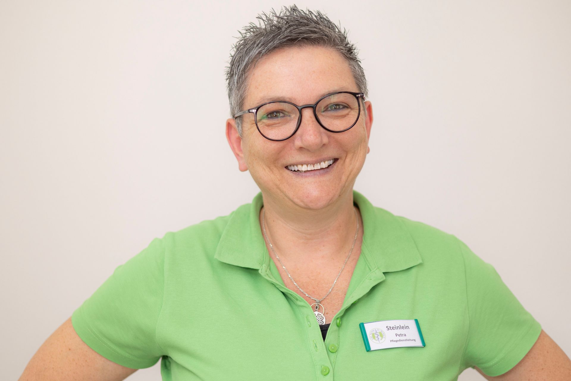 Eine Frau mit Brille und grünem Hemd lächelt in die Kamera.