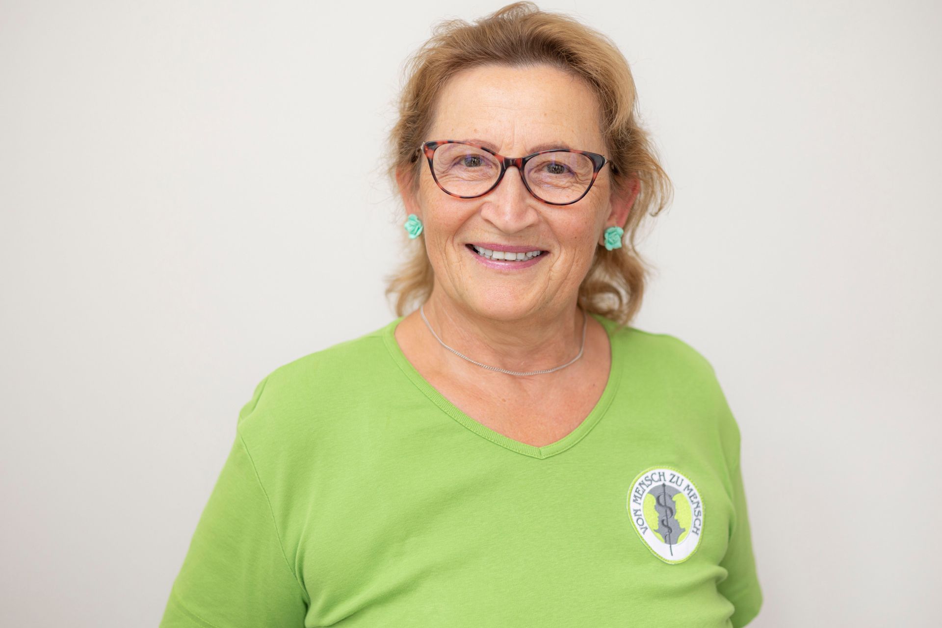 Eine Frau mit Brille und grünem Hemd lächelt in die Kamera.