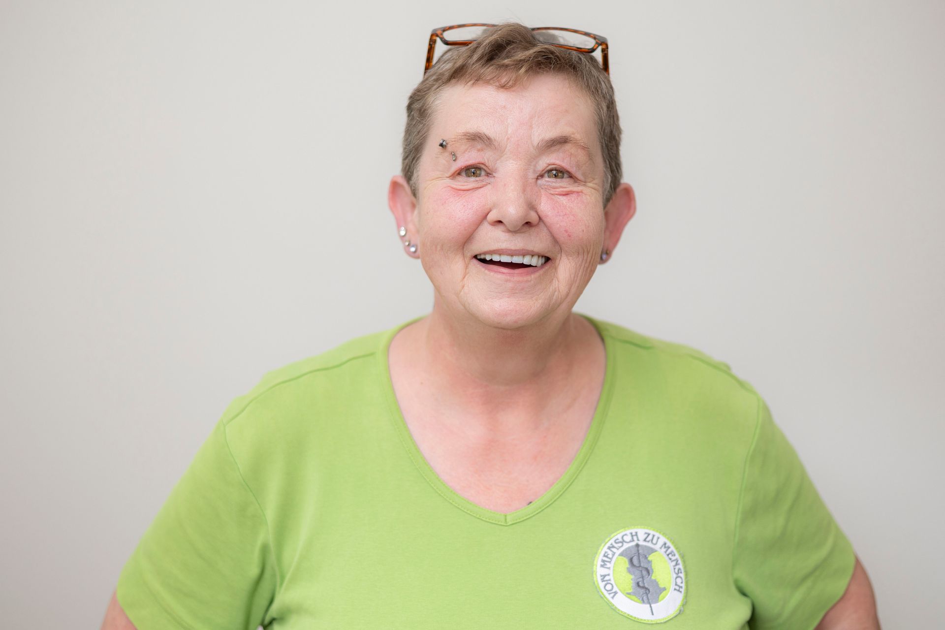 Eine Frau mit grünem Hemd und Brille lächelt in die Kamera.