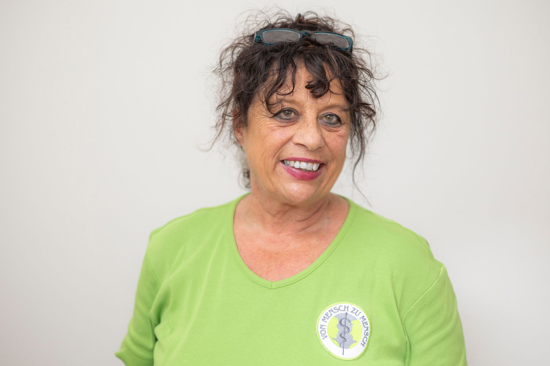 Eine Frau in einem grünen Hemd und einer Sonnenbrille lächelt in die Kamera.