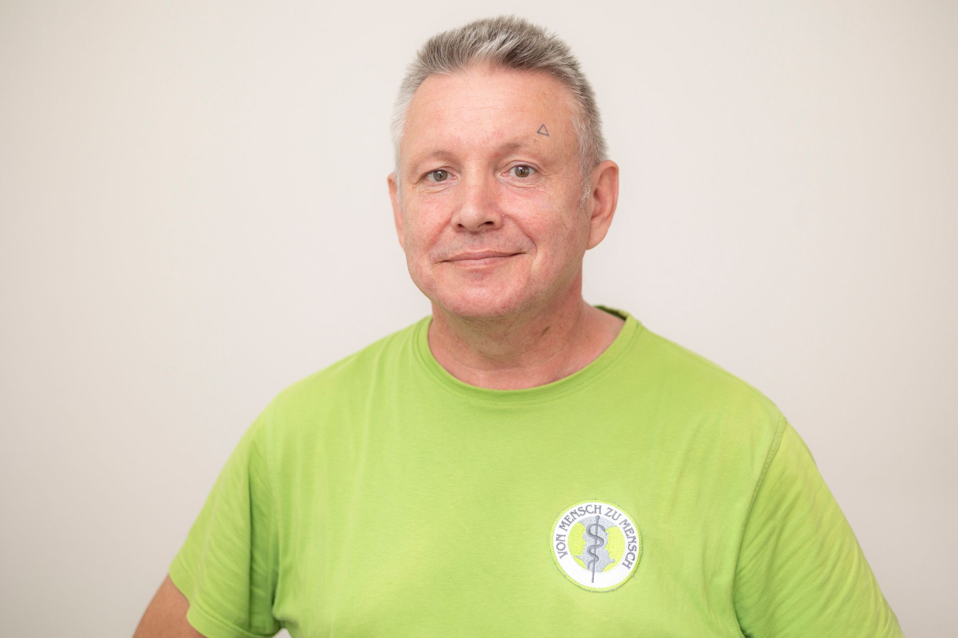 Ein Mann trägt ein grünes T-Shirt mit einem medizinischen Symbol darauf.