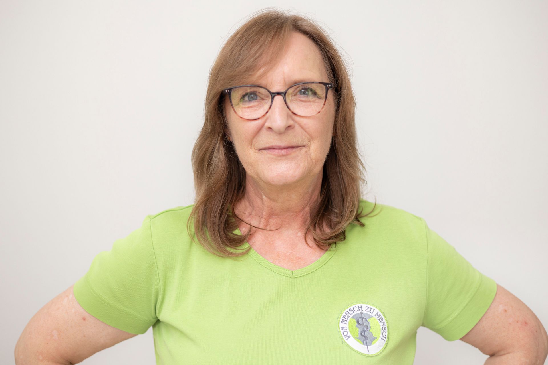 Eine Frau mit Brille und grünem Hemd steht mit den Händen auf den Hüften.