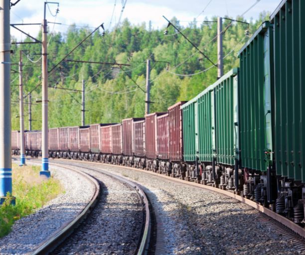 A train is going down the tracks with trees in the background.