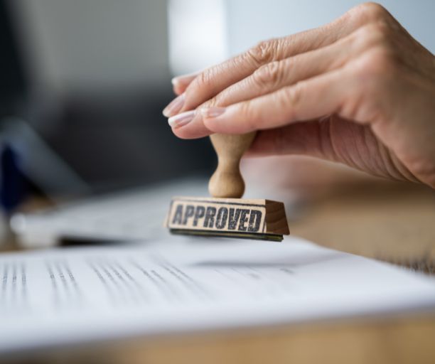 A person is holding a stamp that says approved on a piece of paper.