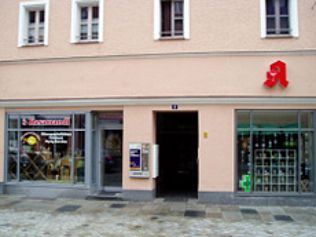 Außenansicht einer Apotheke mit einem roten „A“-Logo und Schaufensterauslagen.