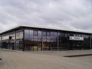 Modernes Gebäude mit großen Glasfenstern, grauer Himmel darüber.