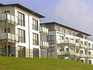 Weiße Wohnhäuser mit Glasbalkonen auf einem grasbewachsenen Hügel.