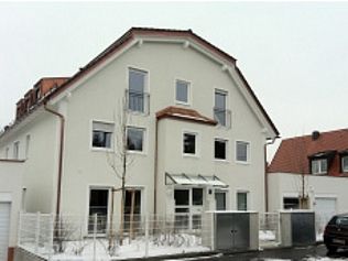 Beiges mehrstöckiges Gebäude mit rotem Dach und roten Fenstern; Schnee auf dem Boden und ein geparktes Auto.