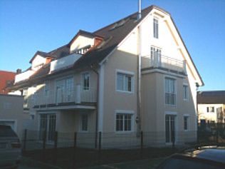 Beiges mehrstöckiges Haus mit dunklem Dach und Balkonen unter einem klaren blauen Himmel.