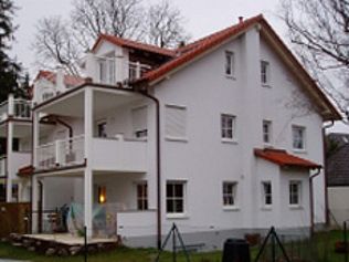 Weißes mehrstöckiges Gebäude mit rotem Dach, Balkonen und Fenstern. Außenaufnahme bei bewölktem Himmel.