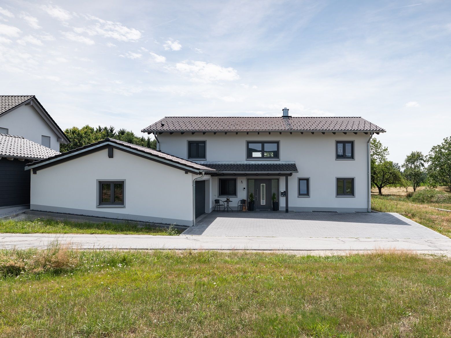 Zweistöckiges hellgraues Haus mit Garage, Auffahrt und grünem Gras. Bewölkter Himmel im Hintergrund.