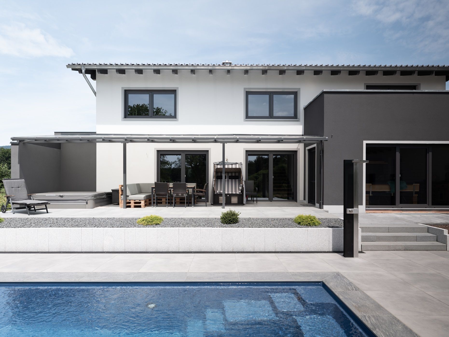 Modernes Haus mit Pool, Terrasse und Pergola. Grau-weiße Außenfassade. Blaues Poolwasser.