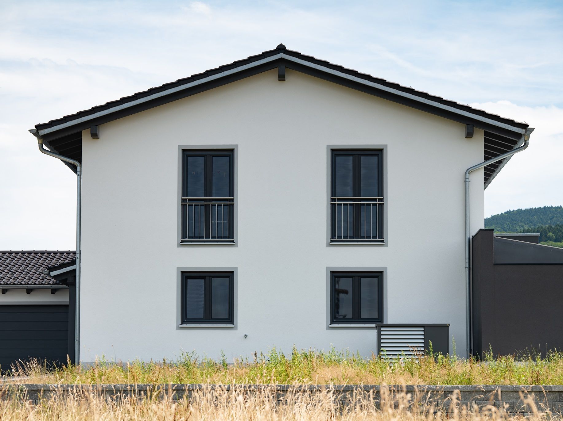 Zweistöckiges weißes Haus mit schwarz gerahmten Fenstern und Dach vor einem blauen Himmel.