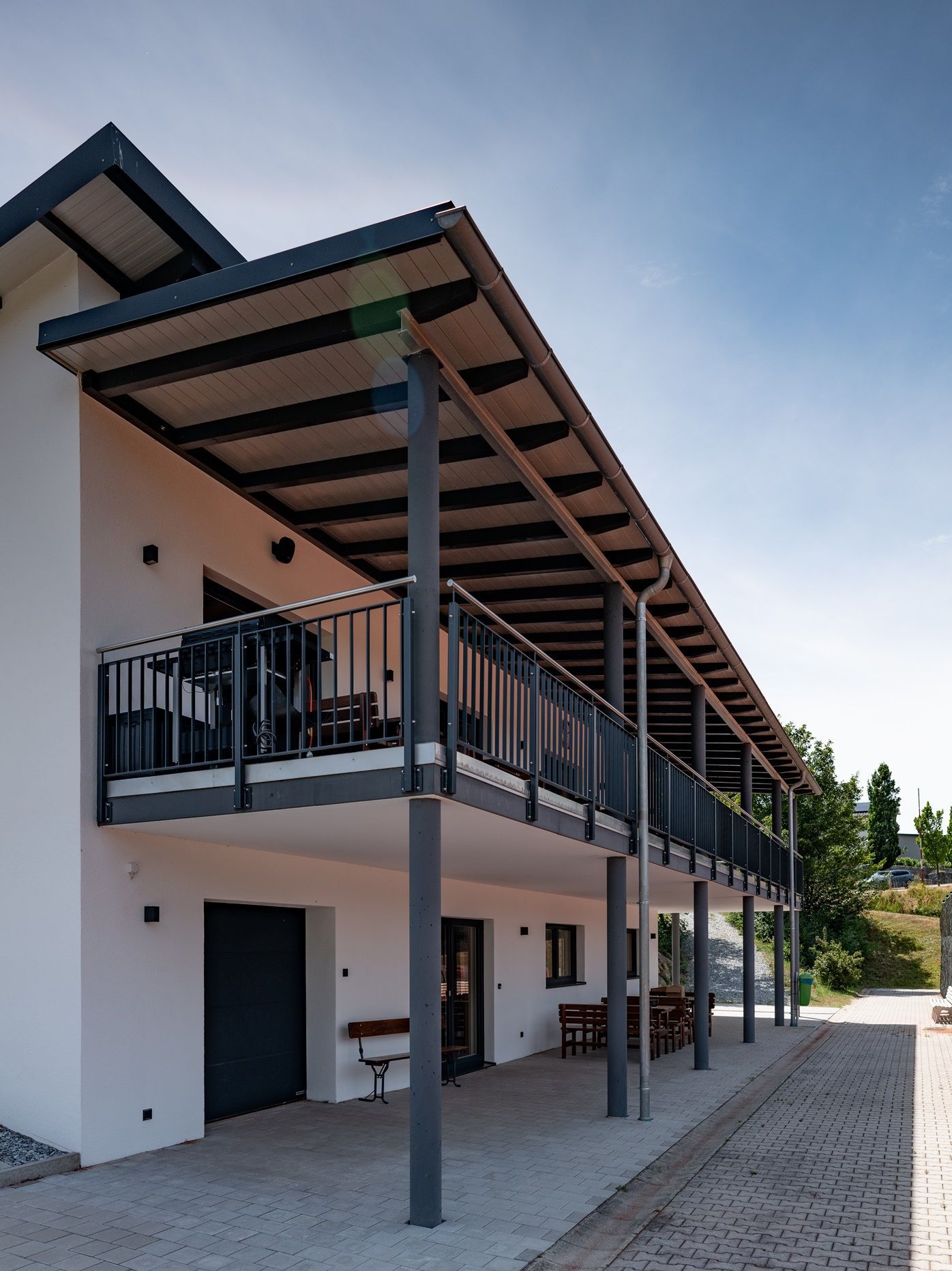 Zweistöckiges, modernes, weißes Gebäude mit einem langen, überdachten Balkon, der von Säulen getragen wird.