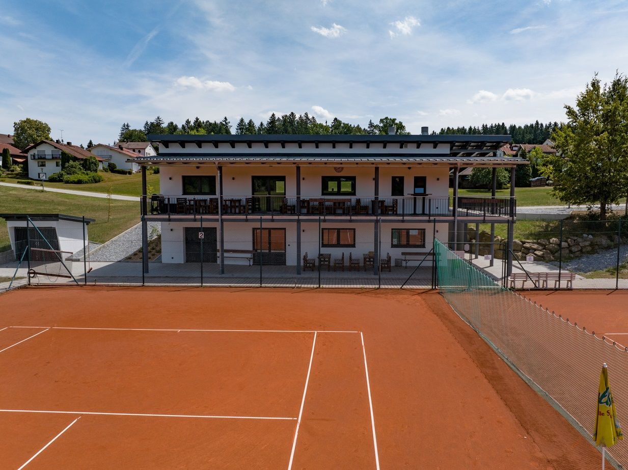 Tennisplatz mit einem zweistöckigen Clubhaus im Hintergrund an einem sonnigen Tag.