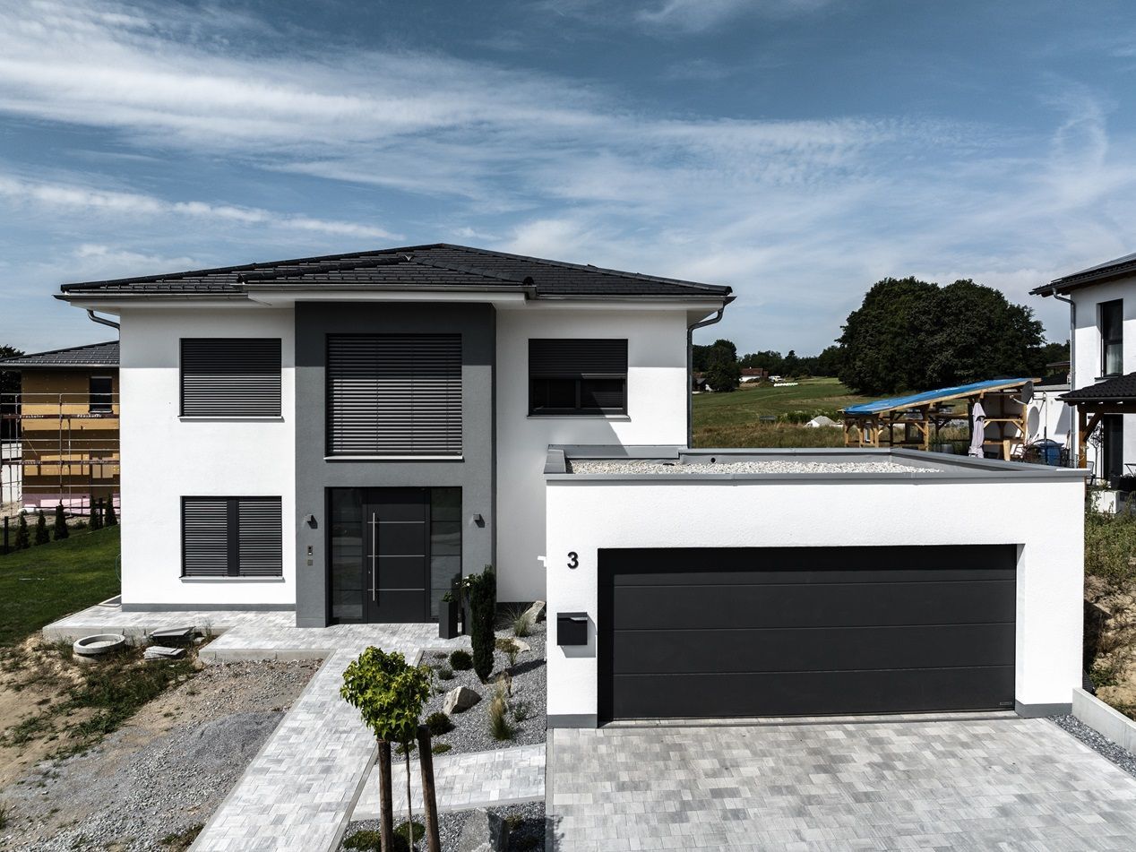 Modernes zweistöckiges Haus mit grauem Garagentor und blauem Himmel im Hintergrund.