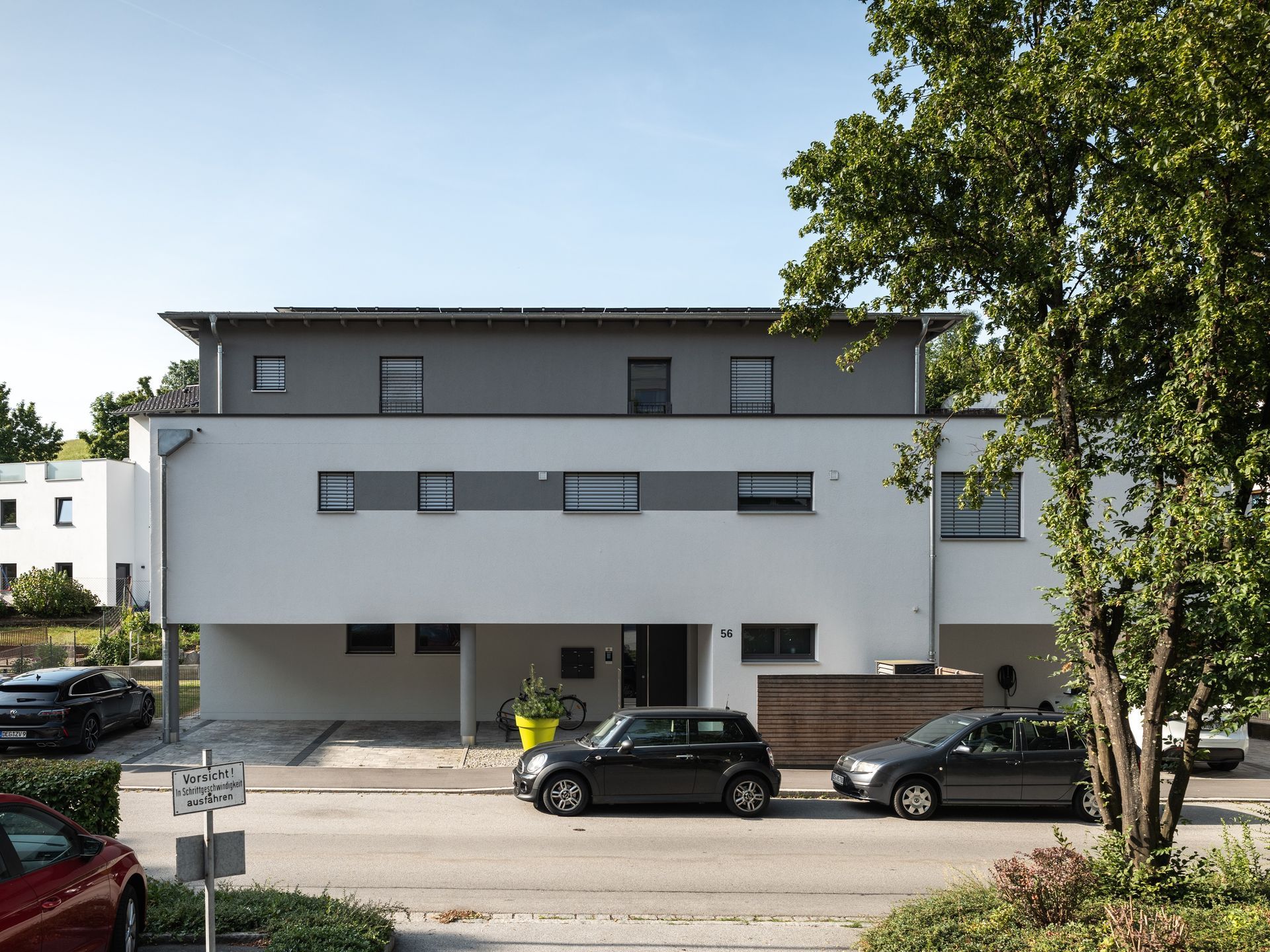 Modernes weiß-graues Gebäude mit davor geparkten Autos. Sonniger Tag.