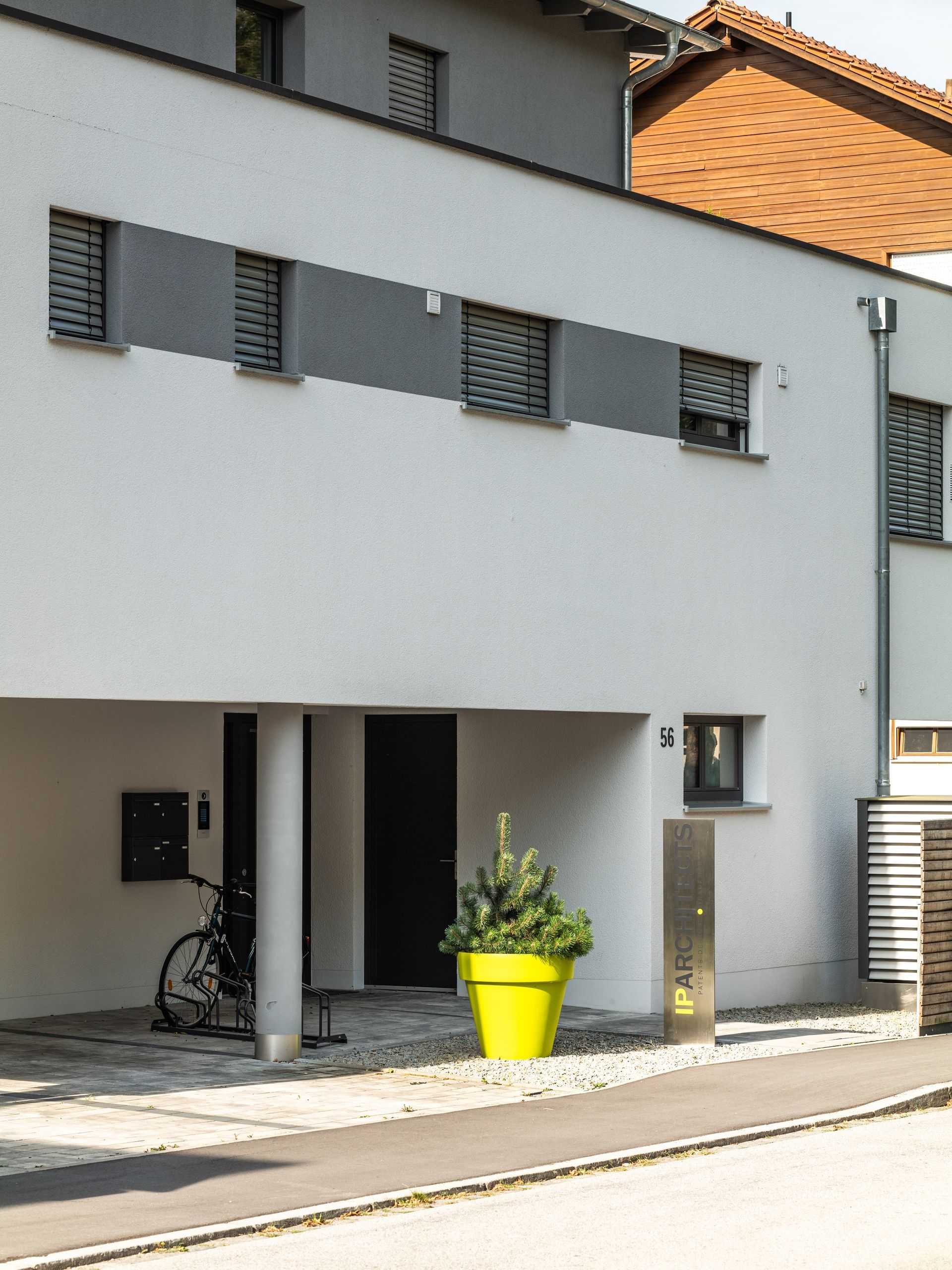 Modernes weißes Gebäude mit grauen Akzenten, Fahrrad und großem gelben Topf mit einer Pflanze.