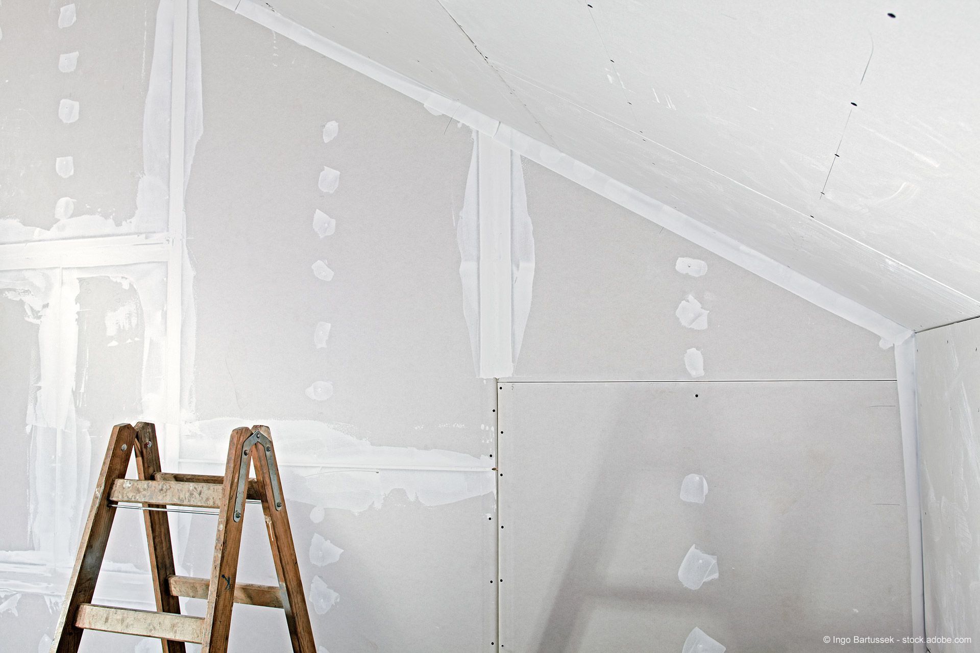 Innenausbauprojekt mit Trockenbauarbeiten unter Verwendung einer Holzleiter. Weiße Wände mit verklebten Fugen und Ausbesserungen.