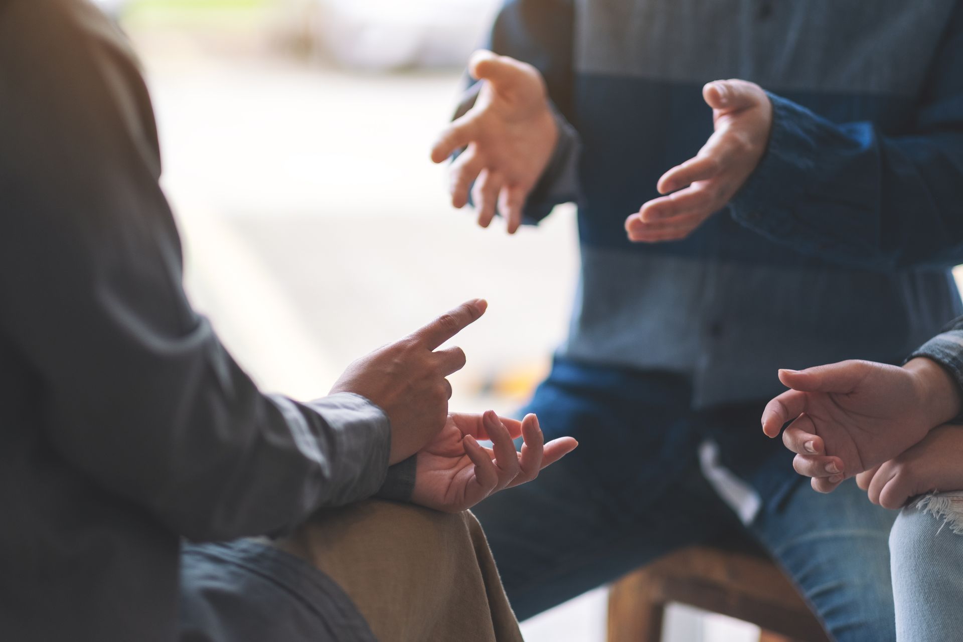 Menschen sitzen in einer kleinen Diskussionsgruppe und gestikulieren mit den Händen in einem hellen Innenraum.