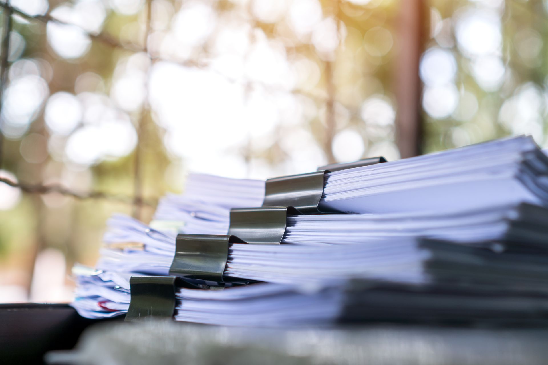 Stapel von Papierakten, zusammengeheftet auf einem Schreibtisch vor einem verschwommenen Hintergrund im Freien